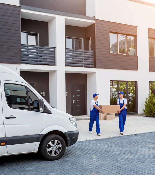 Professional movers carrying moving boxes outside a new home.