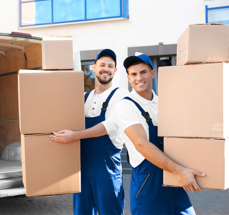 Professional movers carrying moving boxes in a warehouse.