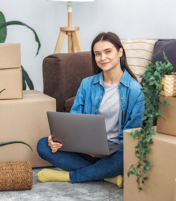 Homeowner using a laptop among moving boxes in a new home.