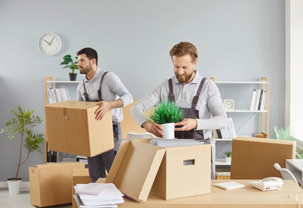 Professional movers carrying moving boxes inside an office.
