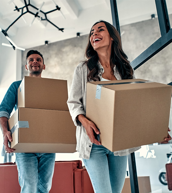 Couple carrying moving boxes into a new home.