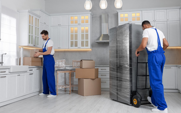 Professional movers carrying moving boxes in a kitchen.