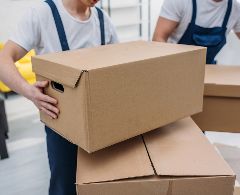 Professional movers lifting moving boxes in a warehouse.