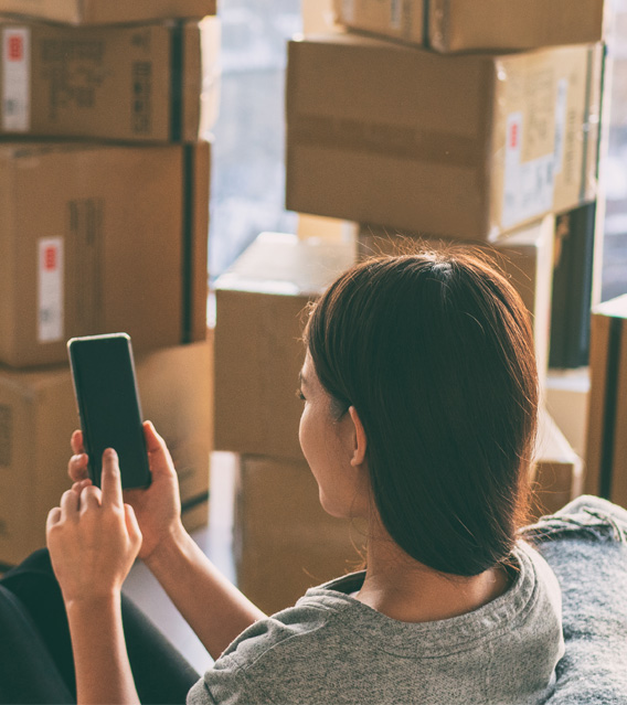 Homeowner using a smartphone among moving boxes after a move.